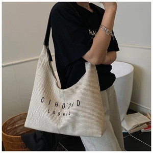 Dettaglio di una grande borsa tote beige intrecciata con tracolla nera e testo grafico