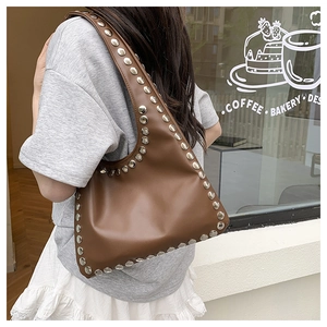 Brown leather tote bag with silver rivets shown on a model in a street style setting