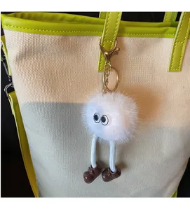Close-up of fluffy white monster keychain charm with long legs on green canvas tote bag