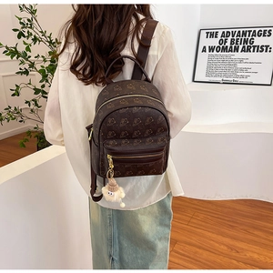 Detailed view of brown mini backpack with bear patterns and white pompom on model