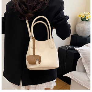 Détail d'un sac seau en cuir grainé blanc cassé avec un charm éléphant marron