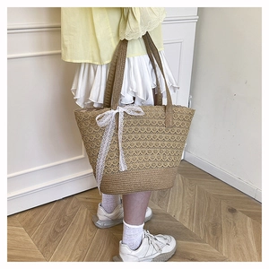 Detail of hand-woven straw tote bag with elegant white lace bow on the front