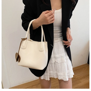 Détail d'un sac seau blanc à motif litchi avec breloque porté par un mannequin