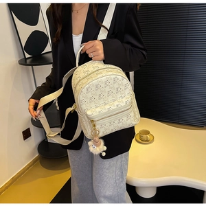 Detail shot of beige mini backpack with cartoon bear prints and plush pendant on model
