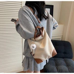 Detailed side view of off-white canvas tote bag with brown leather straps and plush charm