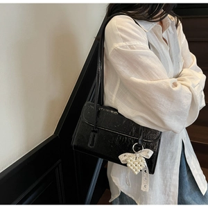 Detail of black wrinkled patent leather shoulder bag with pearl bow heart pendant