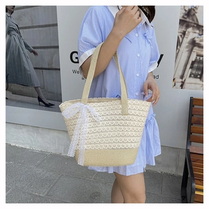 Close-up of beige straw tote bag featuring intricate white lace trim and a bow detail