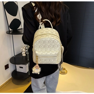 Detail view of beige backpack featuring cartoon bear patterns and pink plush pendant charm