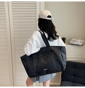 Detail of a large black matte nylon tote bag with wide shoulder strap worn by a model