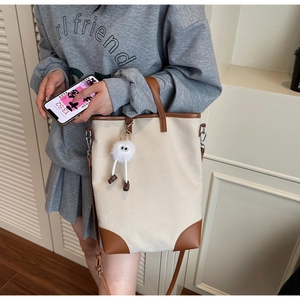 Beige canvas tote bag with brown leather trim and plush charm shown on a model