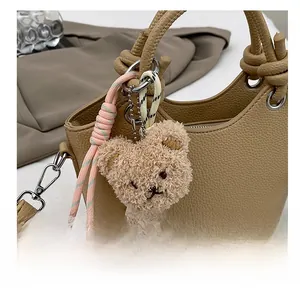 Close-up of fluffy brown bear charm on a khaki leather bucket bag with silver metal ring