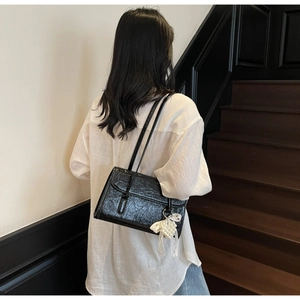 Detail of black wrinkled patent leather shoulder bag with white lace bow charm accessory