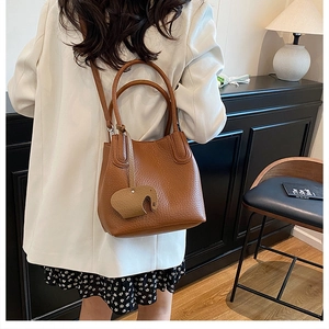 Sac seau marron avec grain de litchi et charm éléphant porté par un mannequin de mode