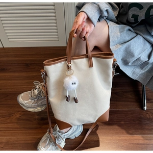 Detail of canvas tote bag with brown leather trim and cute white plush ball charm