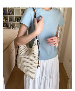 Details der gewebten cremefarbenen Stricktasche mit Holzperlen am Schultergurt