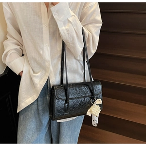 Detail of black glossy pleated shoulder bag with white pearl heart charm and lace ribbon