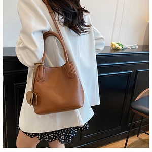 Sac seau en cuir marron avec breloque éléphant porté par un mannequin en blazer blanc