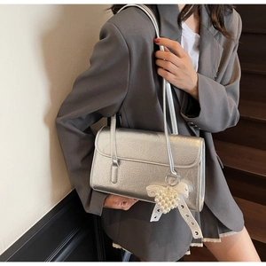 Detail of silver pleated shoulder bag featuring a pearl heart charm on a gray outfit