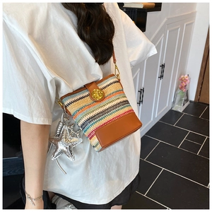 Detail of colorful woven straw bucket bag with brown leather trim and star charm
