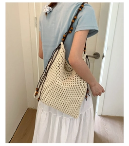 Detail der cremefarbenen Boho-Stricktasche mit dekorativen Schultergurten aus Holzperlen