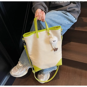 Close-up of beige canvas tote with green faux leather trim and plush monster charm