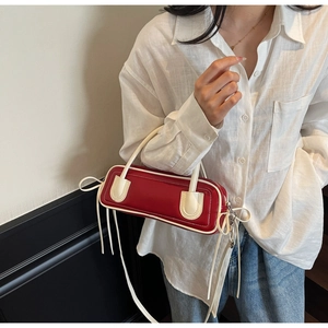 Detail of red baguette bag with ivory piping and long tassel detail on model