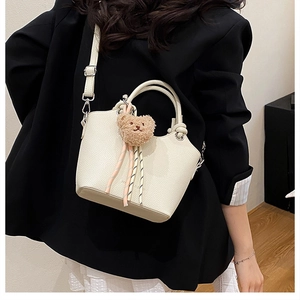 Close-up of beige pebbled leather bucket bag with cute bear charm and knot handle