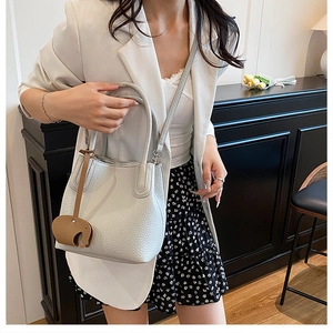 Détail du sac seau blanc à texture litchi avec breloque éléphant marron porté par un mannequin