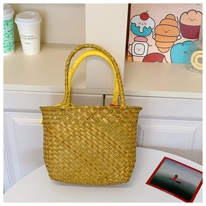 Detail of hand-woven straw beach tote with yellow wrapped handles on a white desk