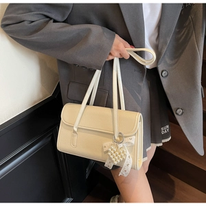 Detail of cream leather shoulder bag featuring pearl heart charm and lace bow decor