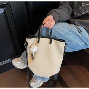 Close-up of beige canvas tote bag with black leather trim and white plush pom-pom charm