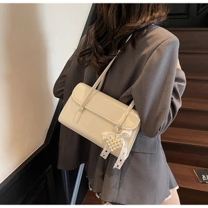 Detail of cream patent leather shoulder bag featuring pearl and lace bow charm on model