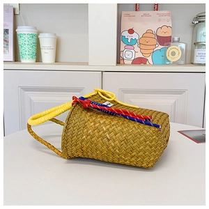 Detail of woven straw bucket bag featuring bright yellow handles and colorful rope ornament