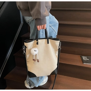 Detail of canvas tote with leather trim and a cute plush monster charm accessory