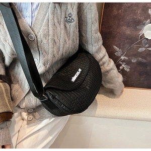 Detail of black quilted crossbody saddle bag with textured nylon and wide shoulder strap
