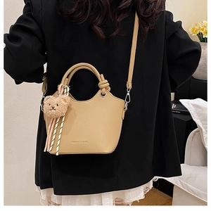 Detail of light brown lychee grain leather bucket bag with plush bear and ribbon accessory