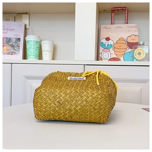 Detail of hand-woven straw bucket bag featuring a yellow drawstring and side label