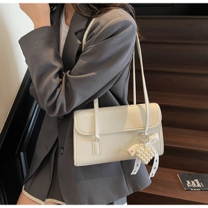 Detail of cream shoulder bag featuring pearl heart pendant and delicate lace bow