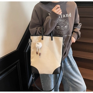 Detail of beige canvas tote bag with black leather trim and cute plush monster charm
