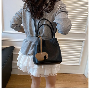 Détail du sac seau noir en cuir grainé avec un pendentif en forme d'éléphant brun
