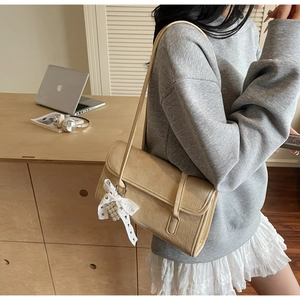 Detail of beige shoulder bag with wrinkled texture, lace bow, and pearl charm detail