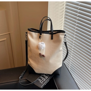 Detail of minimalist canvas tote bag with black leather trim and cute plush doll charm