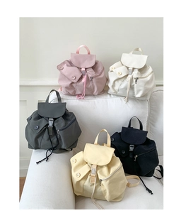 Detailed view of casual drawstring backpacks in five colors on a white fabric sofa