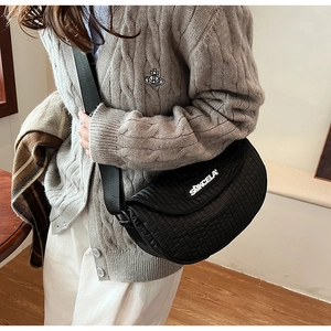 Detail of black quilted crescent saddle bag with logo print and wide shoulder strap