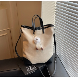 Detail view of canvas tote bag with leather trim and cute plush doll charm accessory