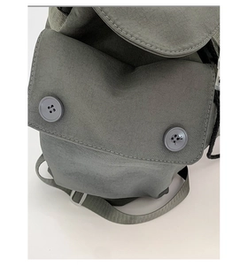 Detailed macro view of nylon backpack front pocket with dual button closure and metal buckle