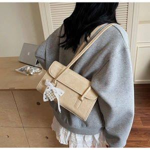 Close-up of beige shoulder bag featuring a lace bow and pearl charm with soft leather texture