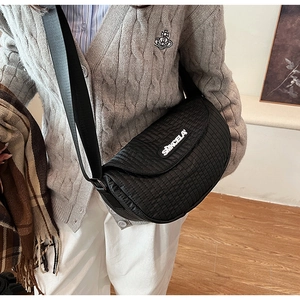 Close-up of a black quilted crescent crossbody bag with white logo and soft texture