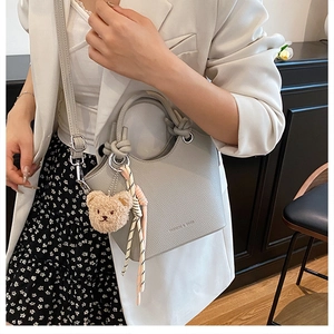 Litchi texture bucket bag detail with knot handle, teddy bear charm and striped scarf