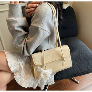 Detail of beige pleated leather shoulder bag with a lace bow pearl charm on a model